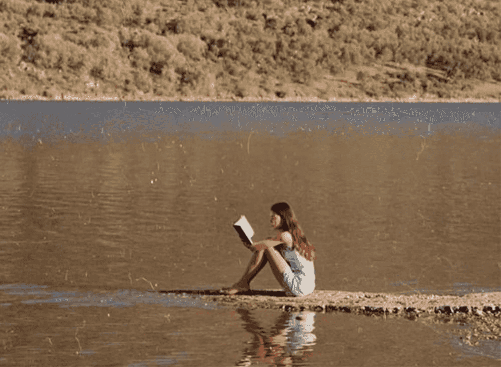 woman reading book next to water